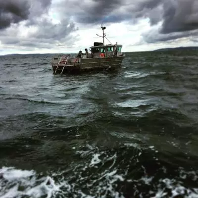 A fishing boat in open water, with two people on the deck. The sky has dark clouds, and there are waves.